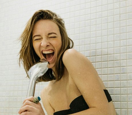 Eine Frau benutzt den Duschkopf als Mikrofon und singt
